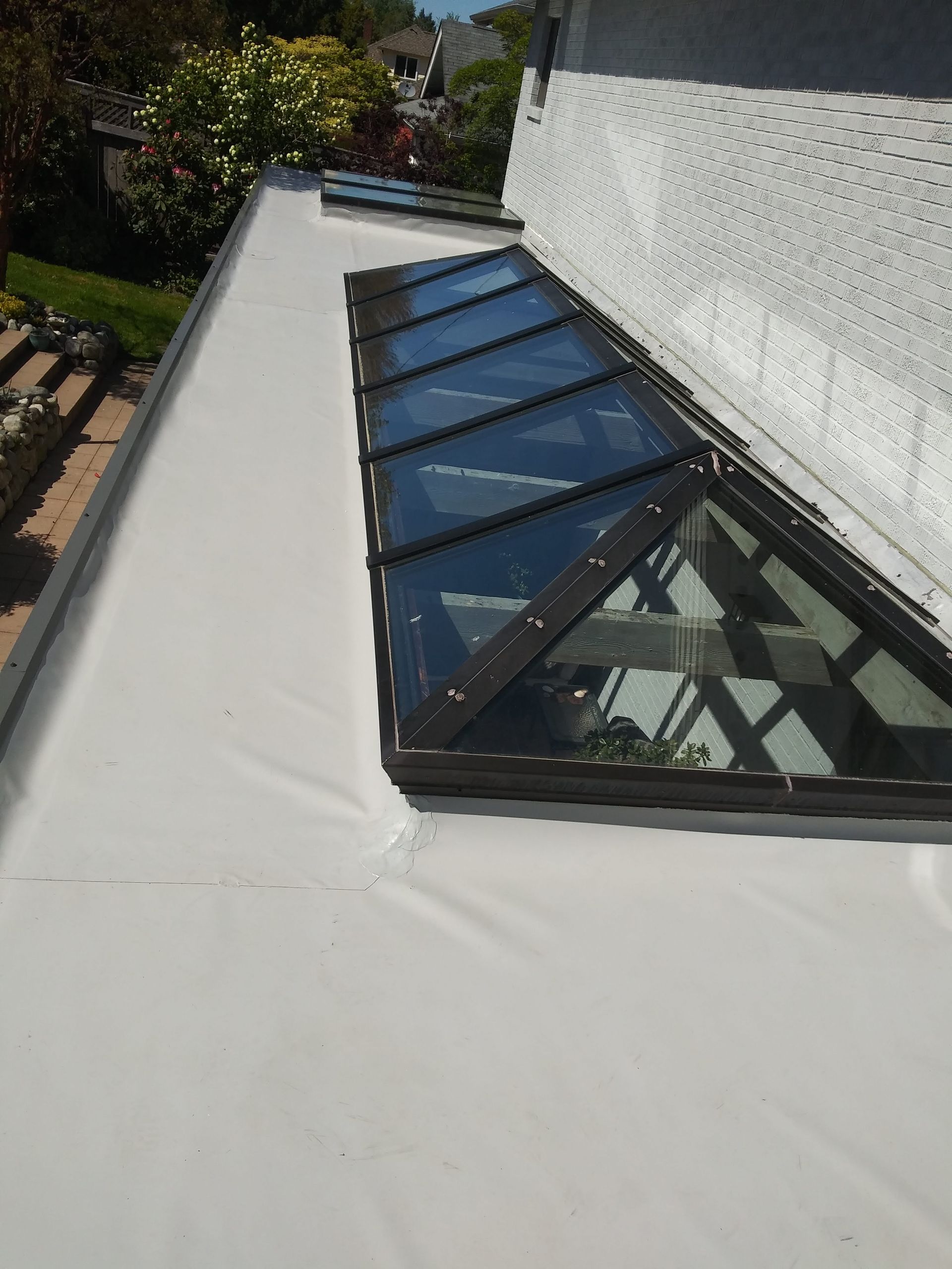 Flat white rooftop with a row of black-framed glass skylights beside a white wall.