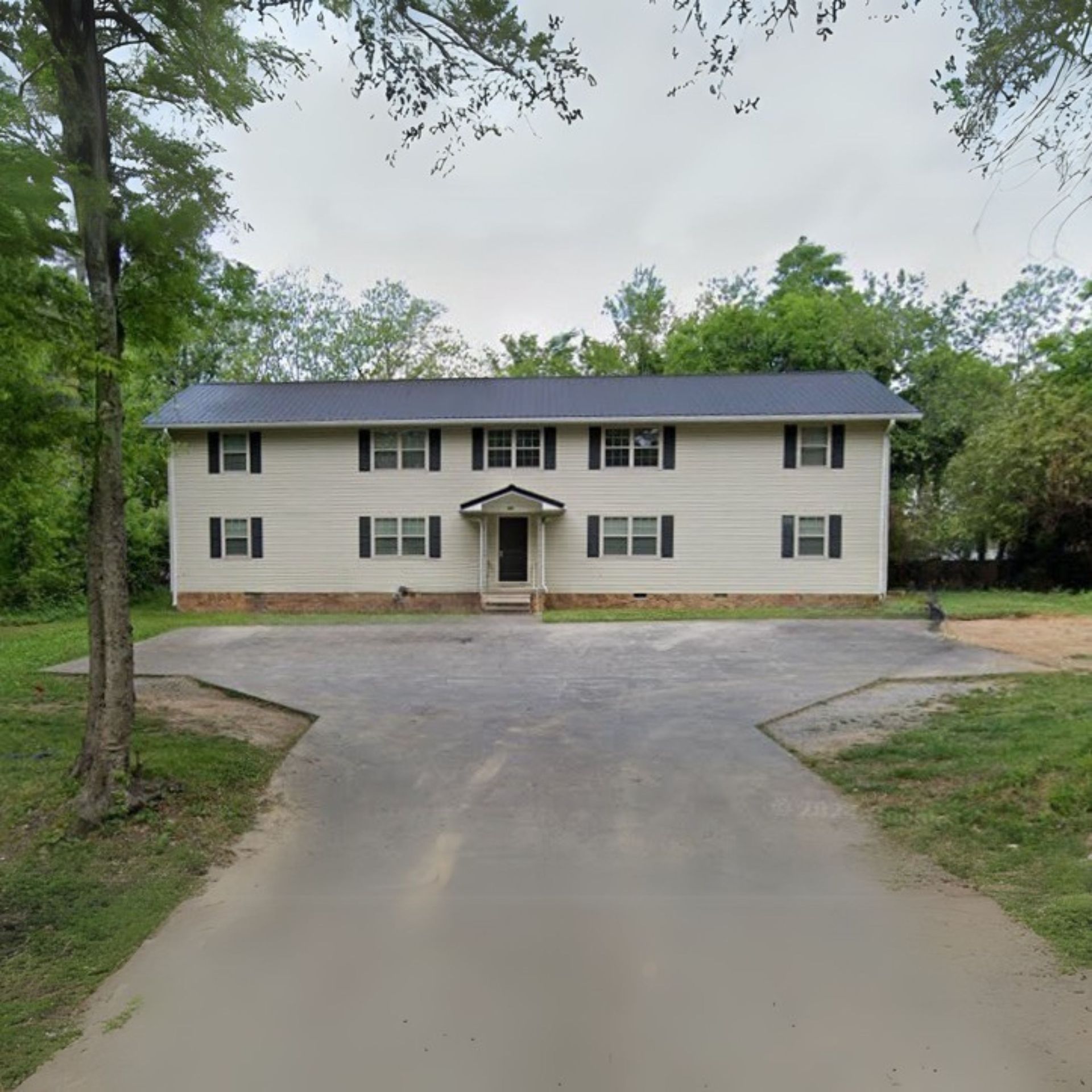 A white house with black shutters is surrounded by trees and grass