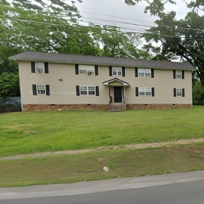 A white house with black shutters sits in the middle of a lush green field
