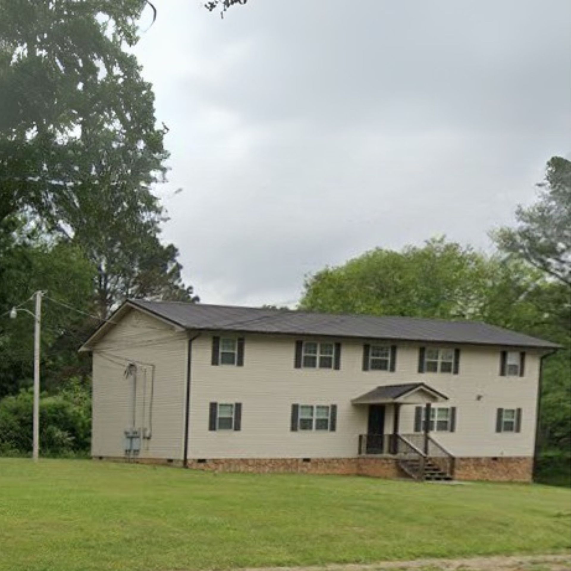 A large white house with a black roof is surrounded by trees and grass.