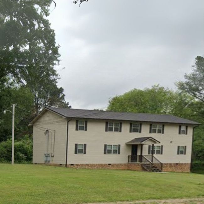 A large white house with a black roof is surrounded by trees and grass.