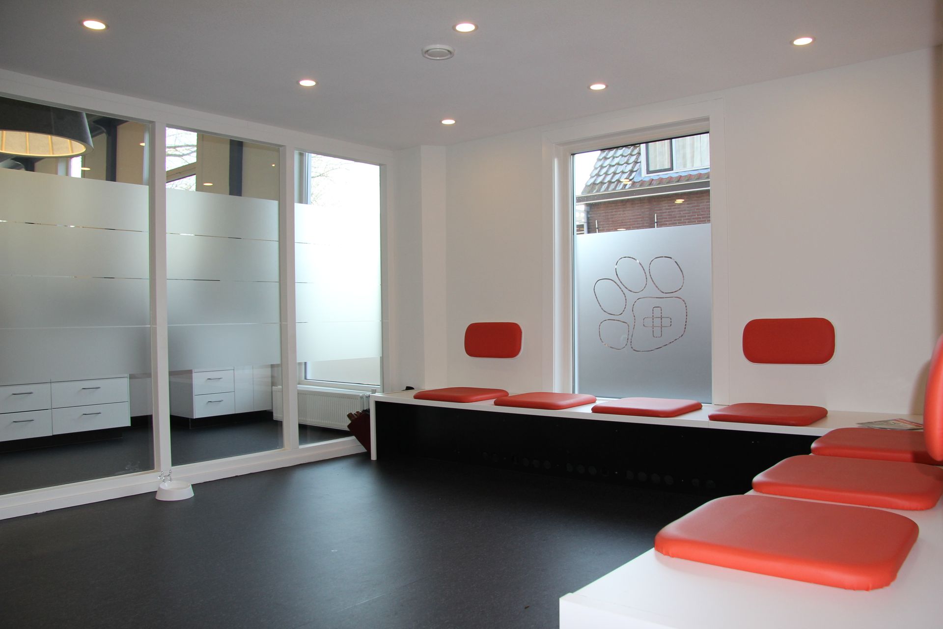 Moderne wachtkamer met rode stoelen, scheidingswanden van matglas en een donkere vloer.