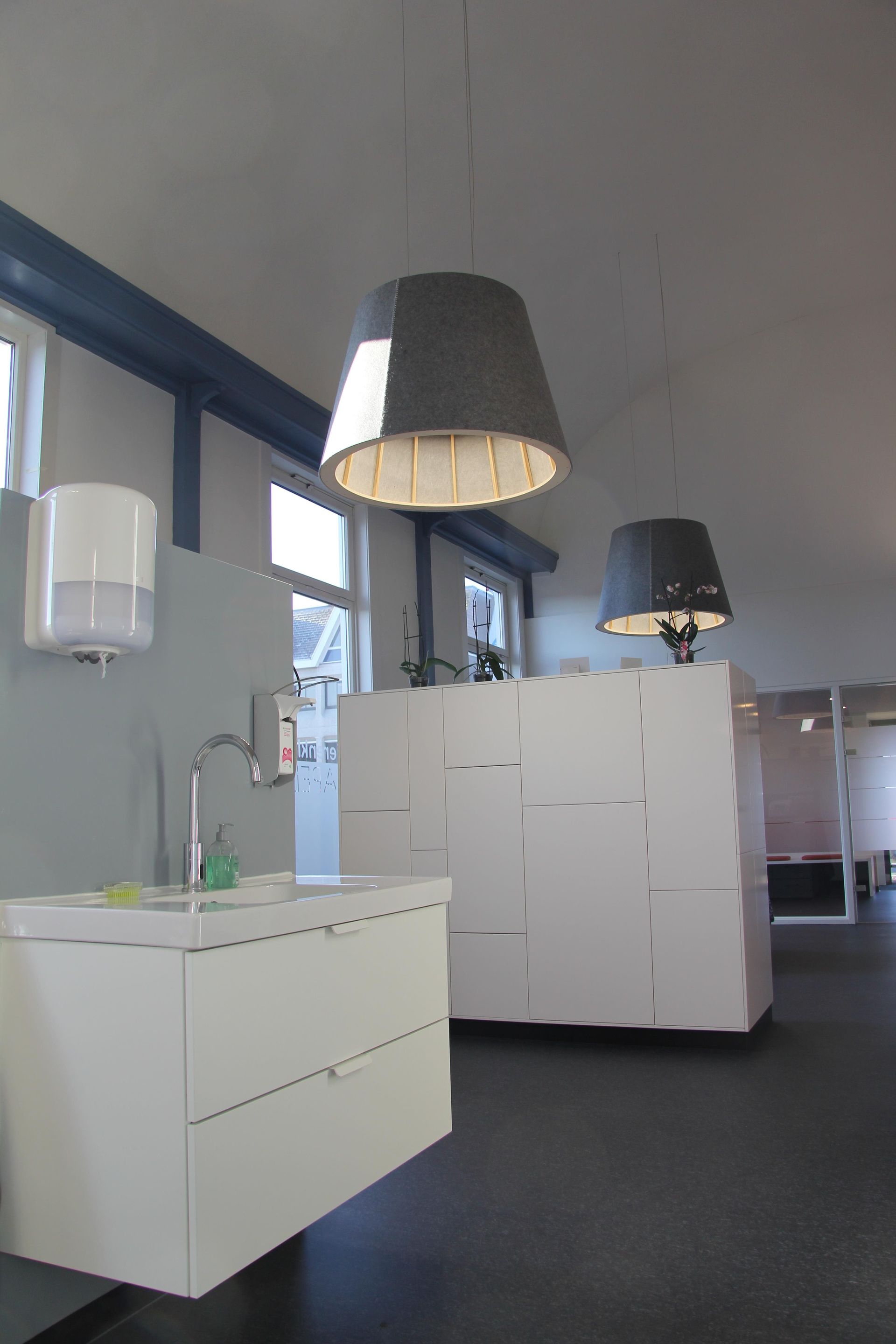 Modern kantoorinterieur met witte kasten, hanglampen en een donkere vloerbedekking.
