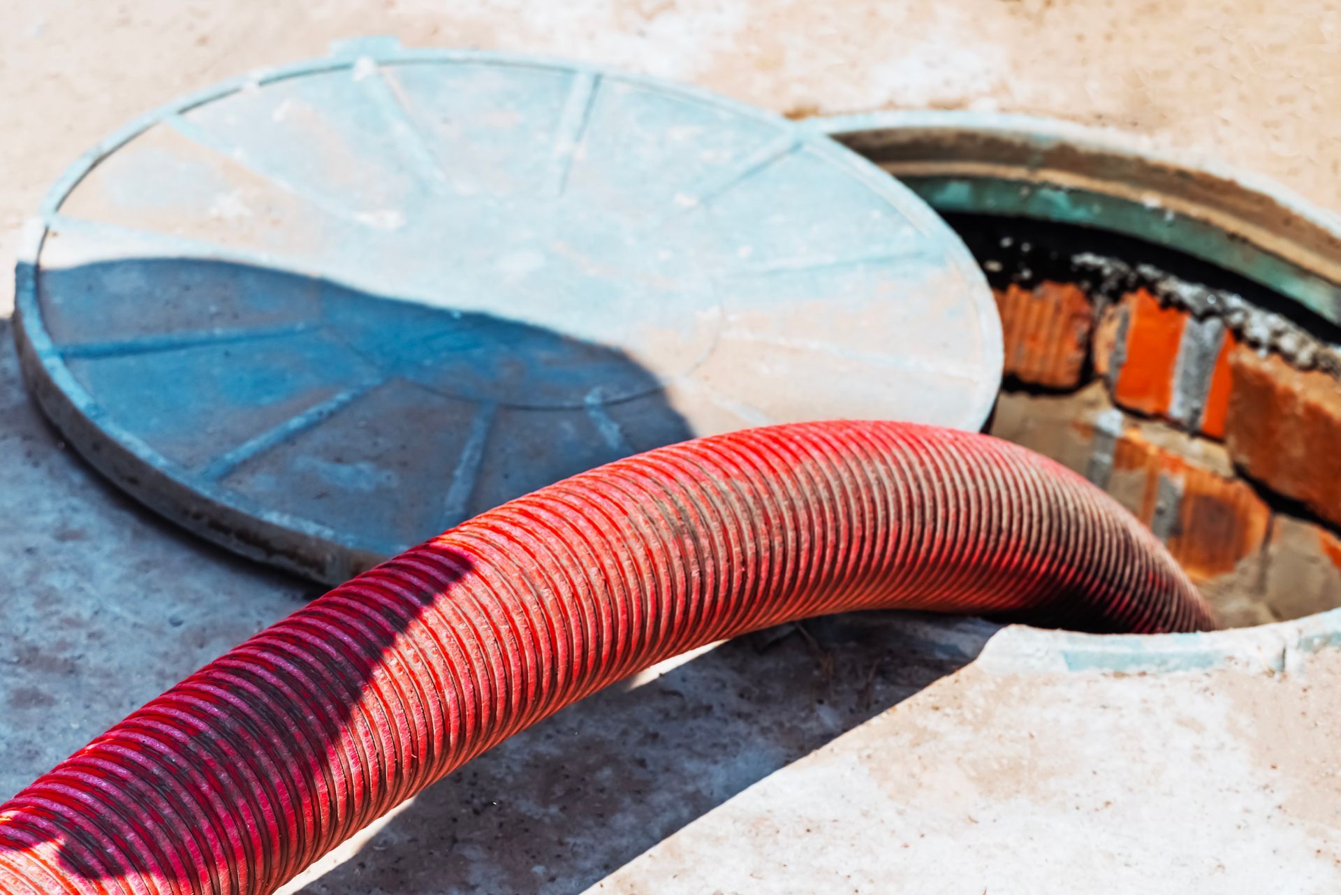 A red hose is coming out of a manhole cover.