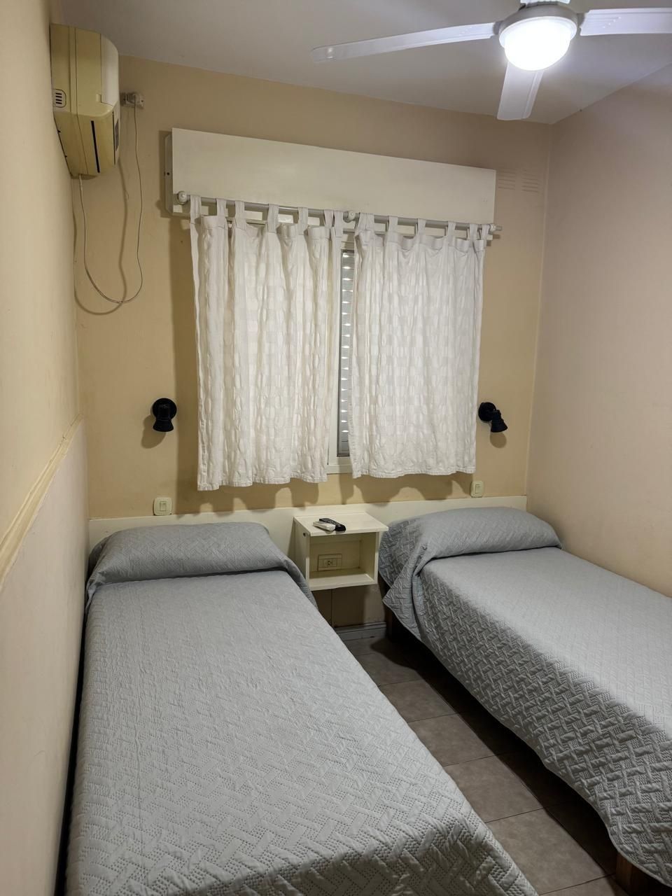 Dos camas individuales con colchas grises estampadas en una habitación con una mesita de noche central