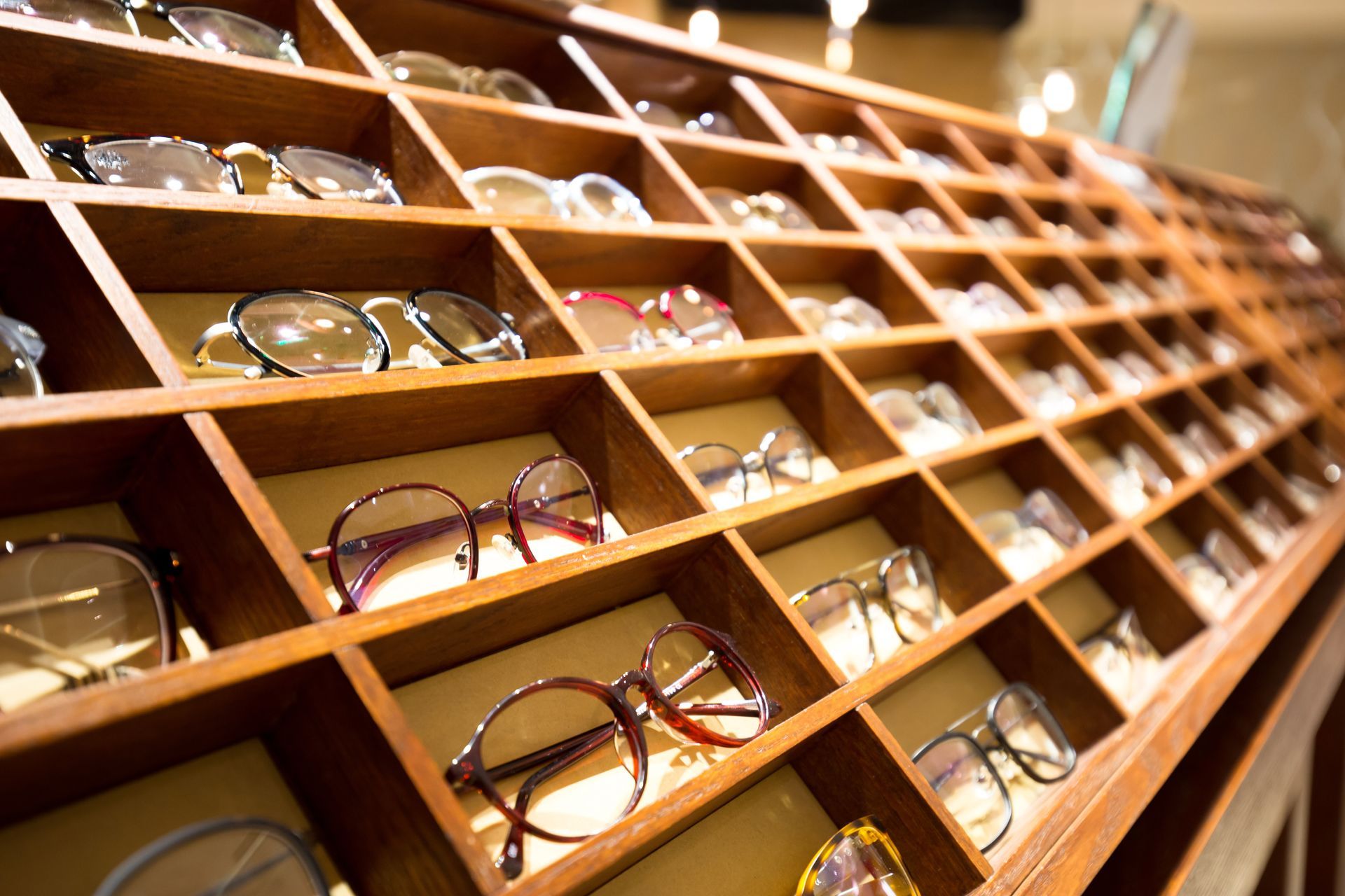 Rows of eyeglasses displayed in wooden shelves inside a store
