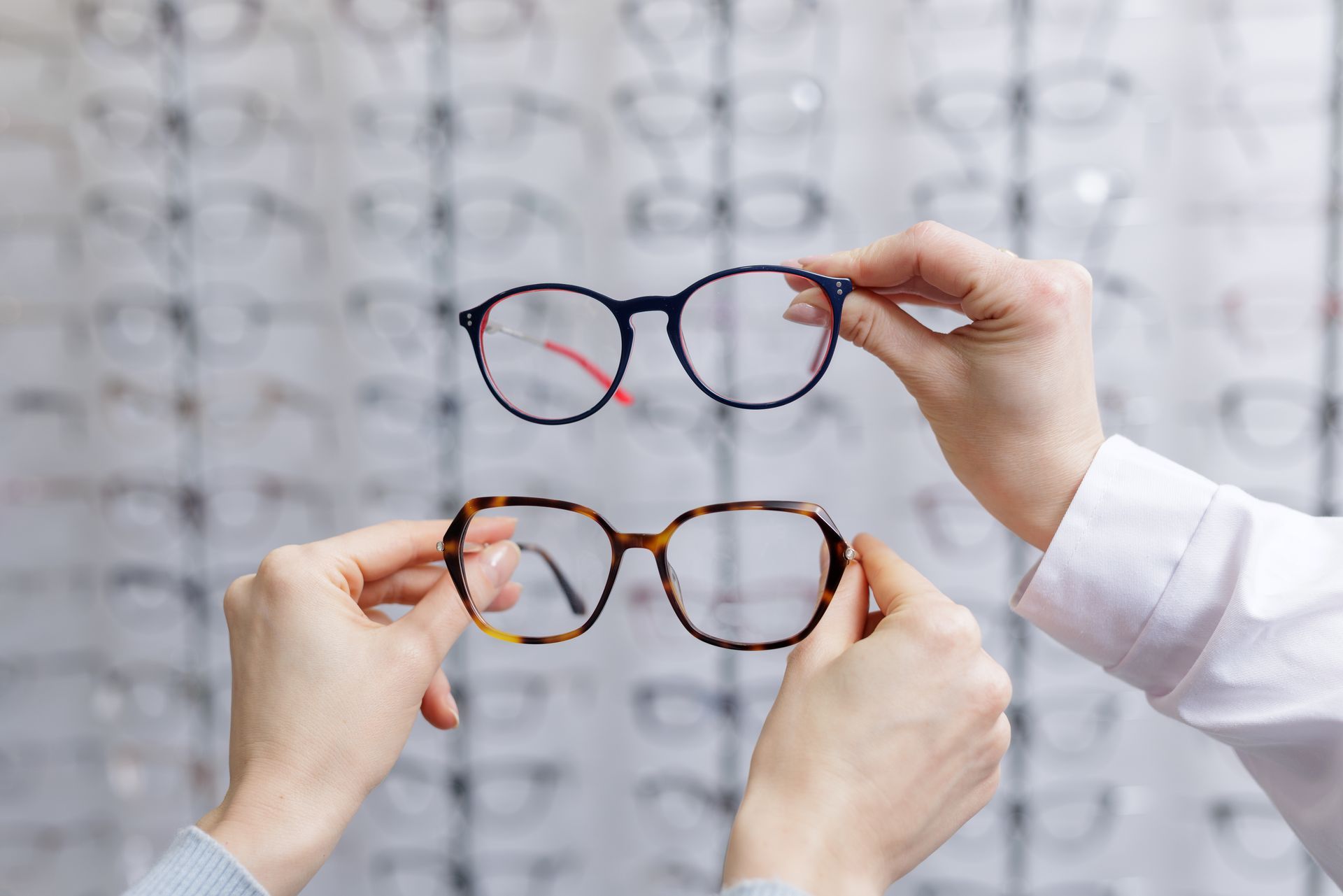Hands holding two pairs of eyeglasses in front of an eye chart Hands holding two pairs of eyeglasses in front of an eye chart