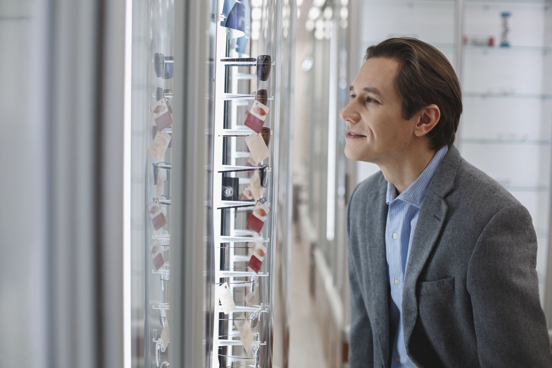 Man in a gray blazer looking into a glass display case in a bright indoor setting