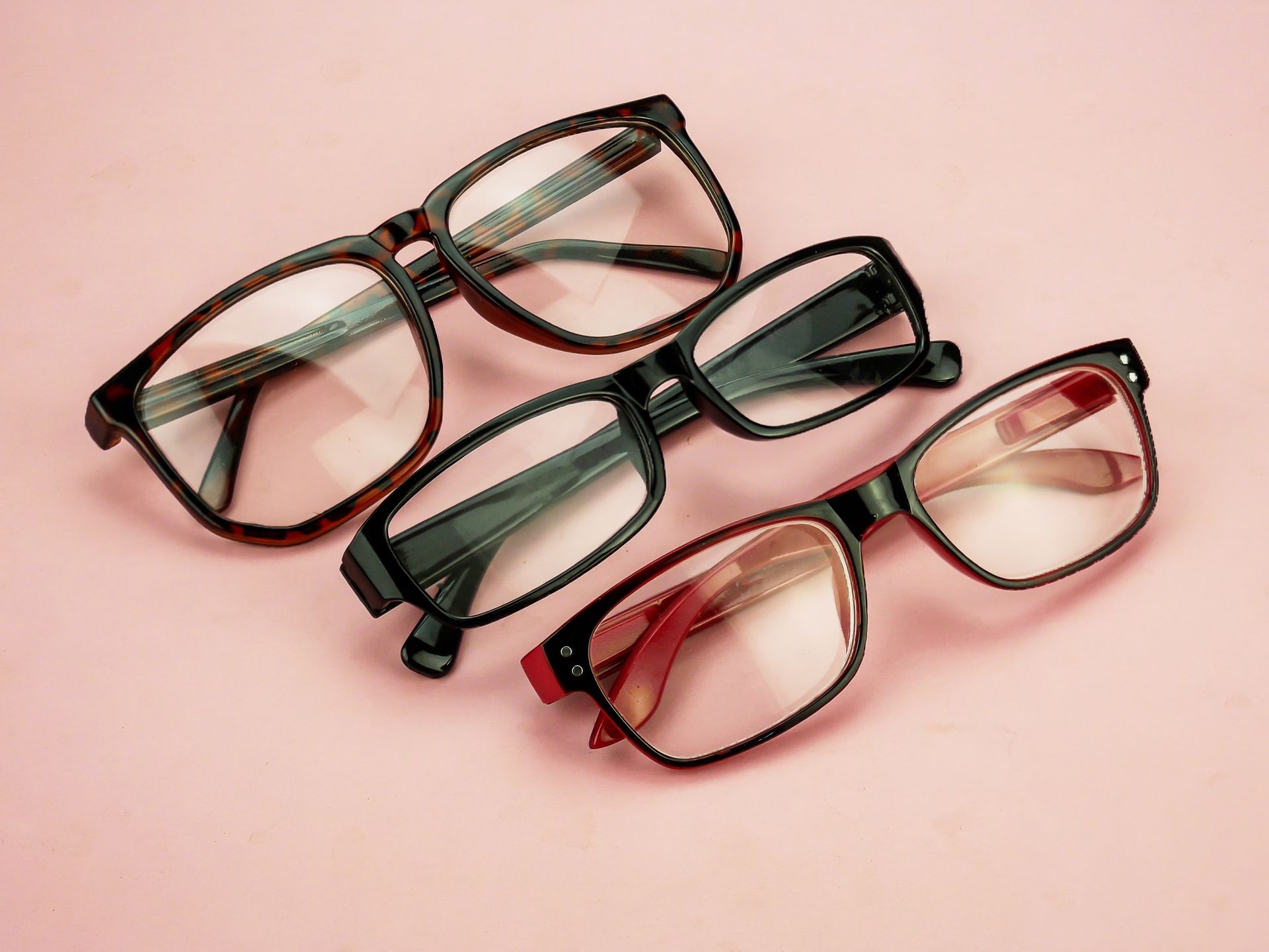 Four pairs of eyeglasses in black, red, and brown frames on a pink background