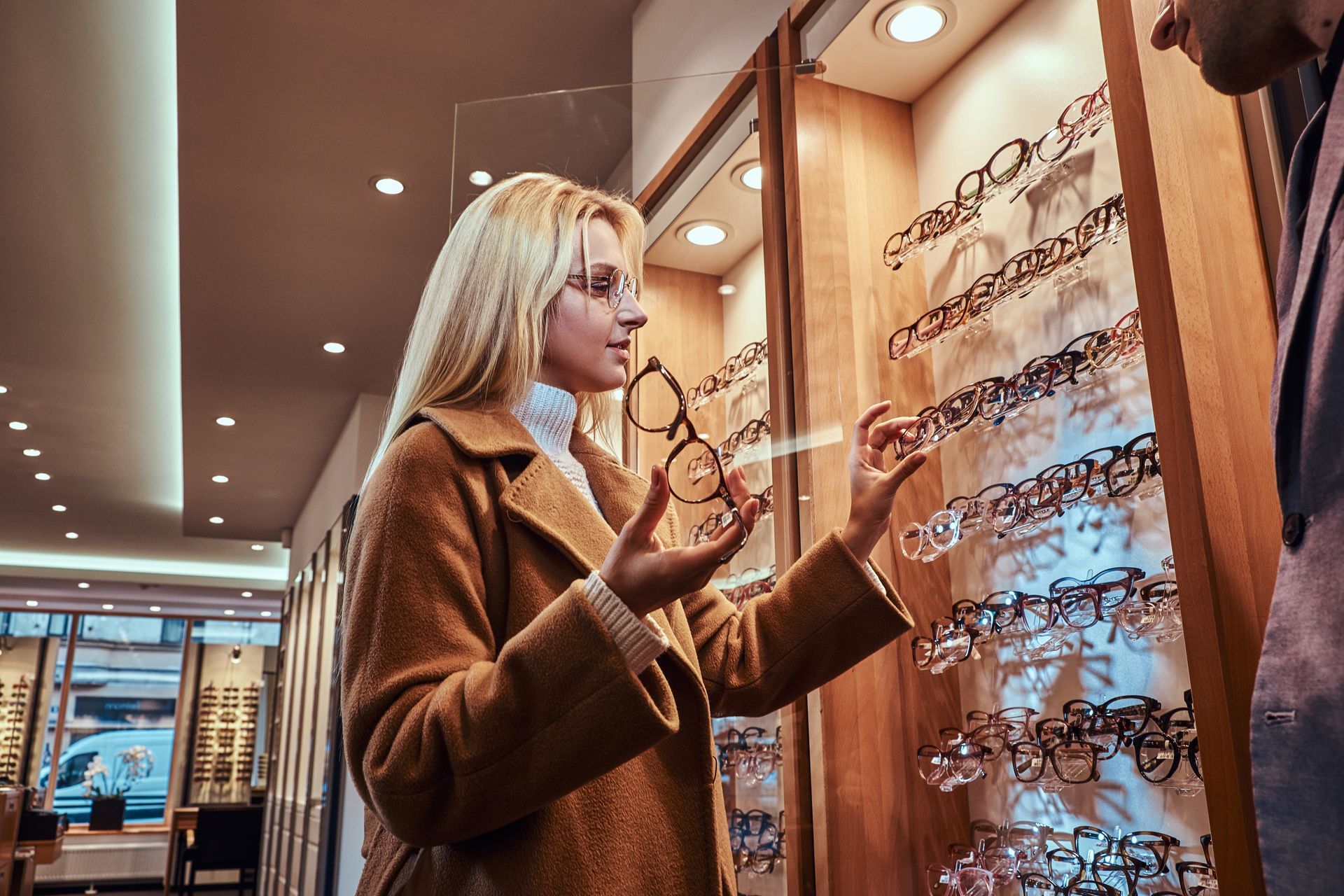 Woman browsing eyeglass frames in a warmly lit optical store