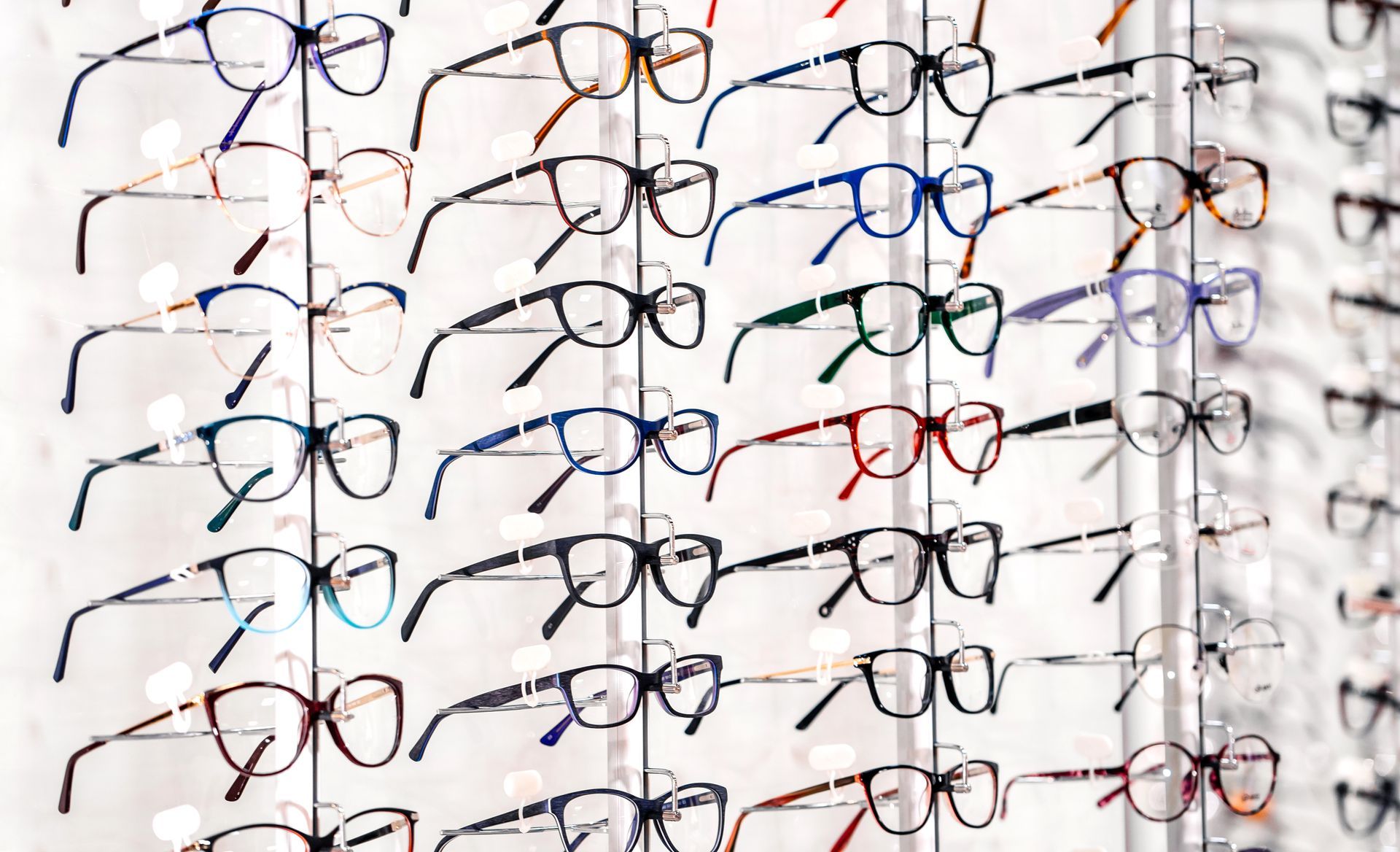 Rows of eyeglasses in various frame colors displayed on a white wall rack.