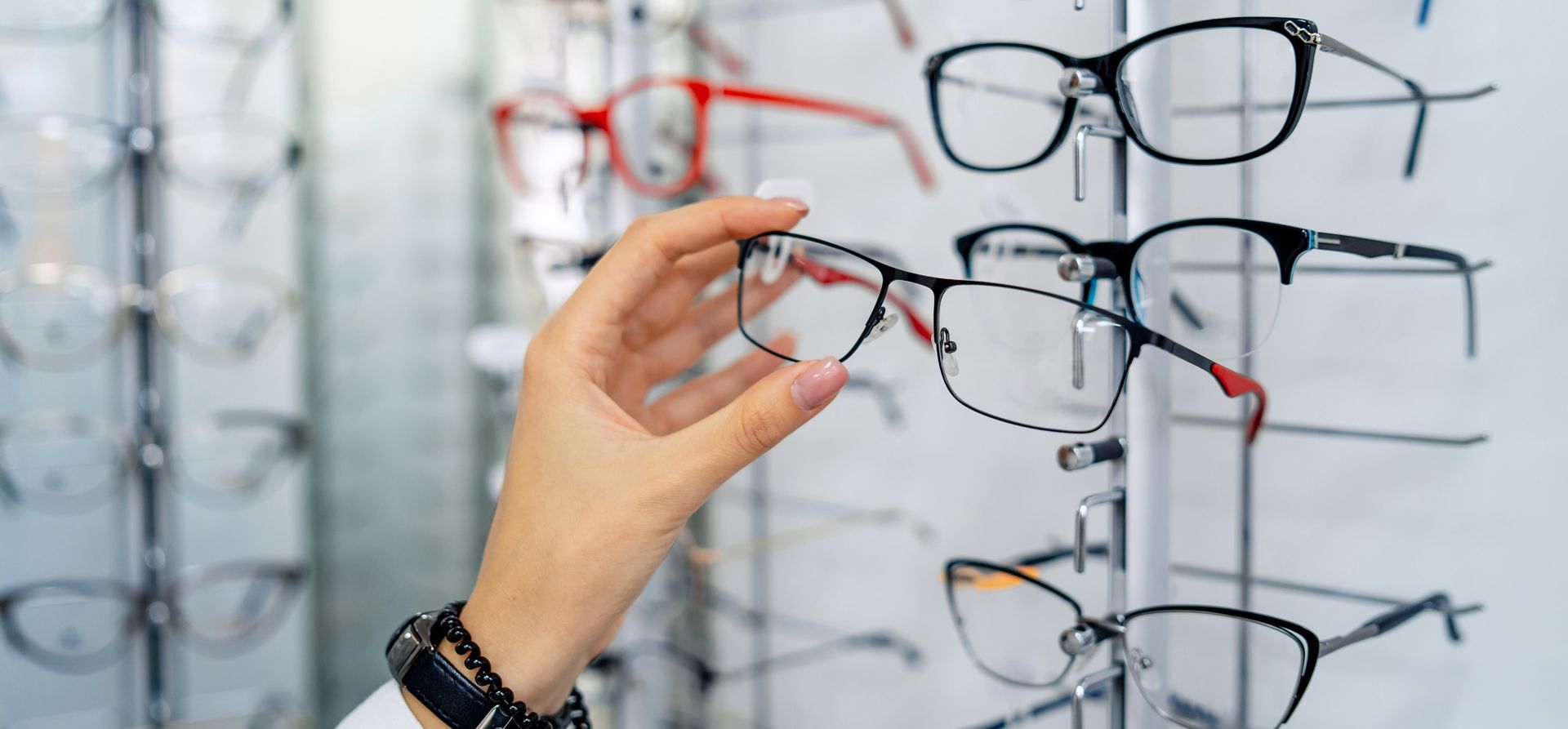 Hand selecting eyeglass frames on a display wall in an optical shop