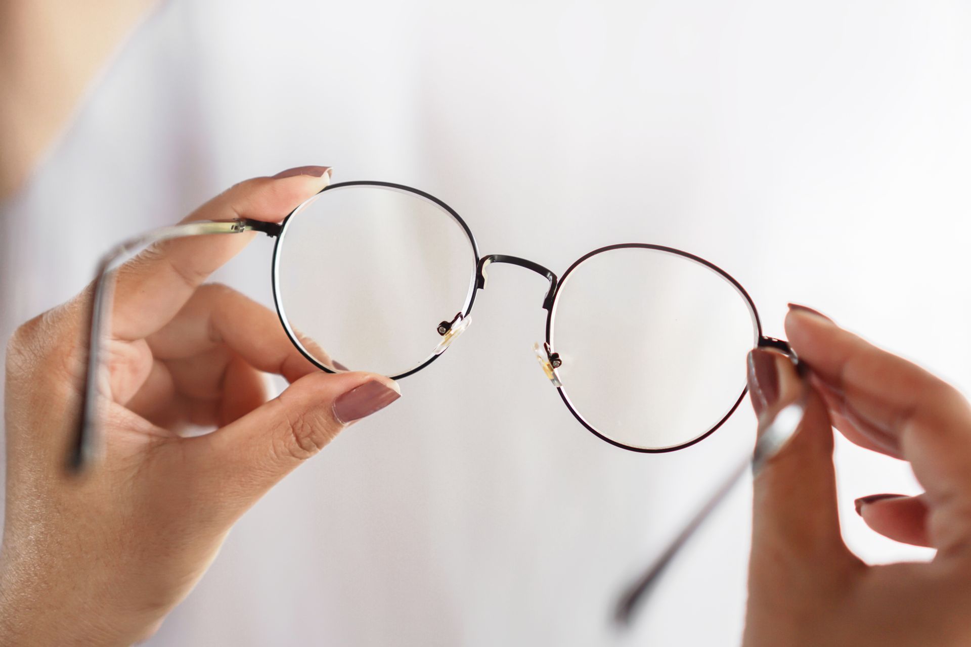 Hands holding round eyeglasses against a blurred background