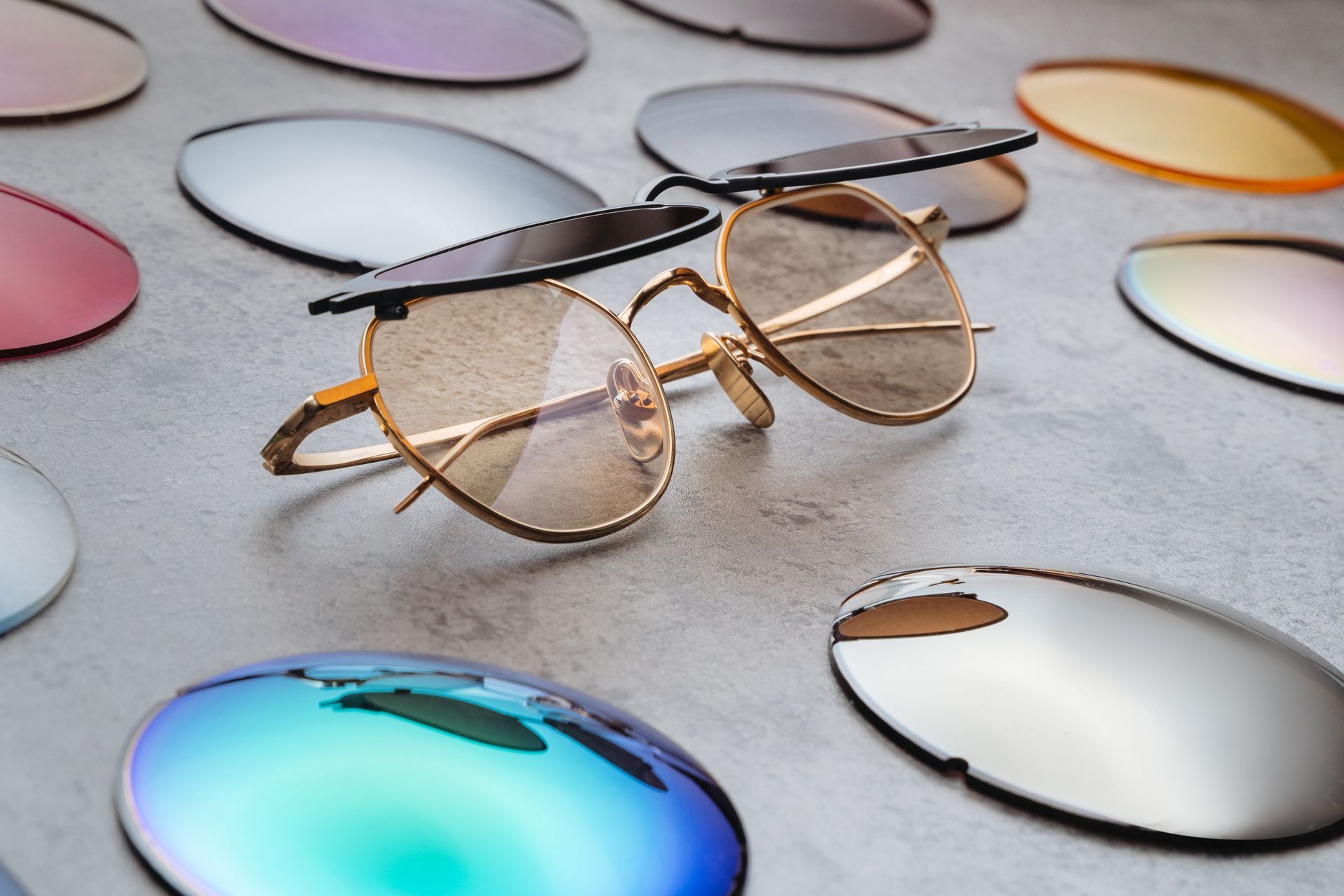 Gold eyeglasses on a gray surface with colorful reflective lenses and scattered lens caps