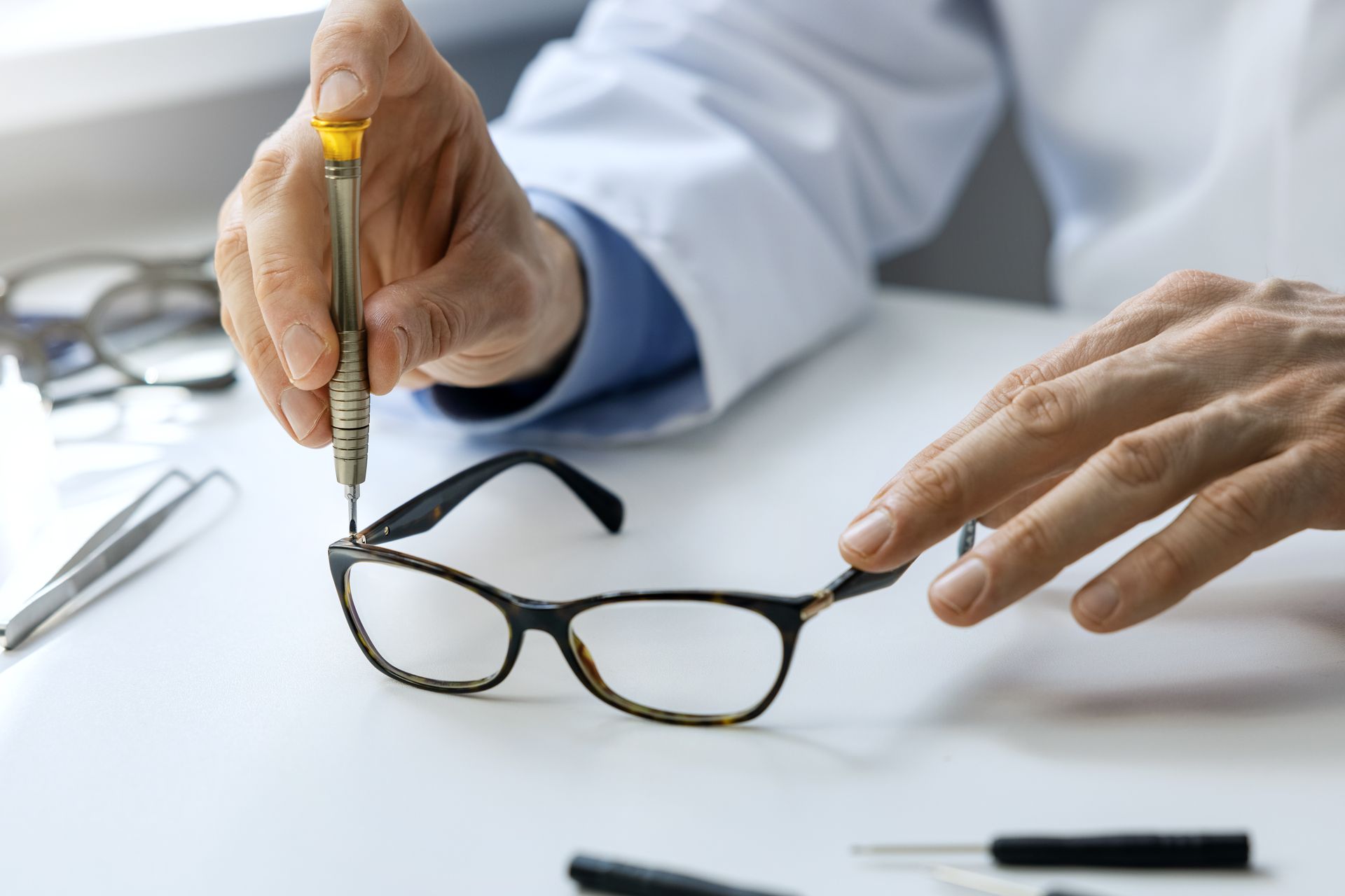 Hands adjusting eyeglasses on a white desk with a pen and clipboard nearby