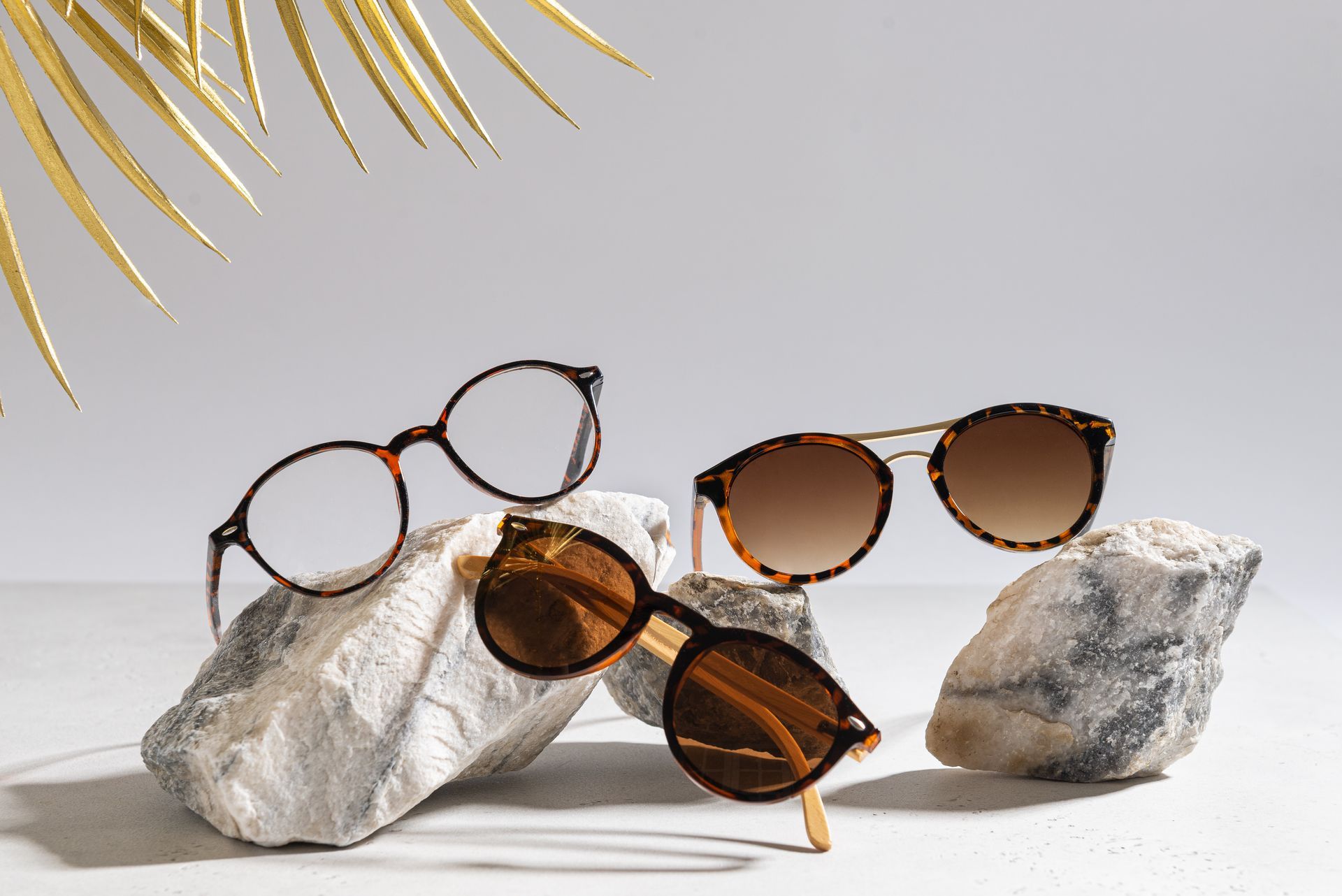 Three pairs of sunglasses displayed on white rocks against a light gray background.