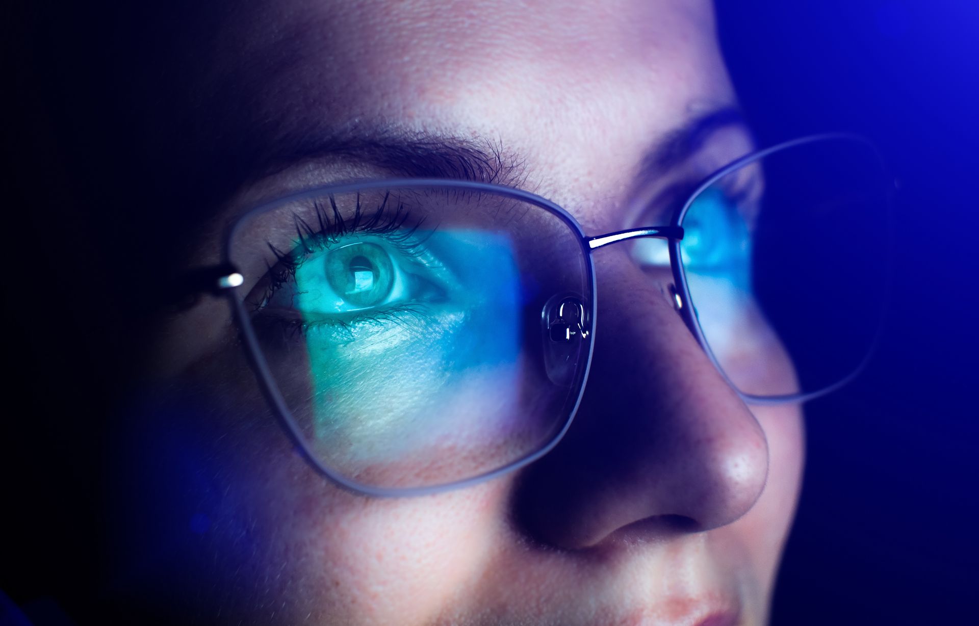 Close-up of a person wearing glasses, lit by blue and purple neon reflections on the lenses