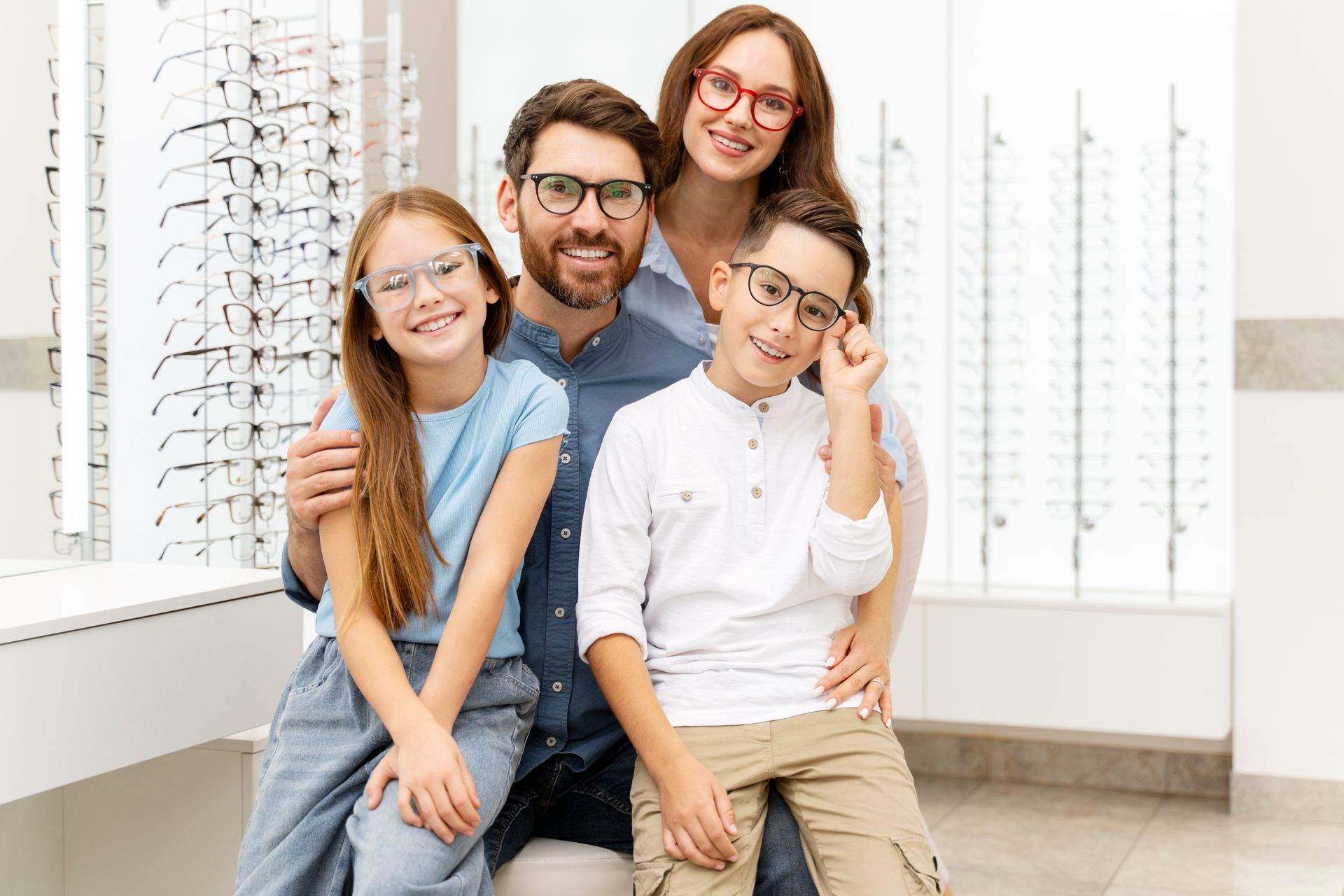 Family of four smiling in an eyeglasses shop, seated together in front of display racks