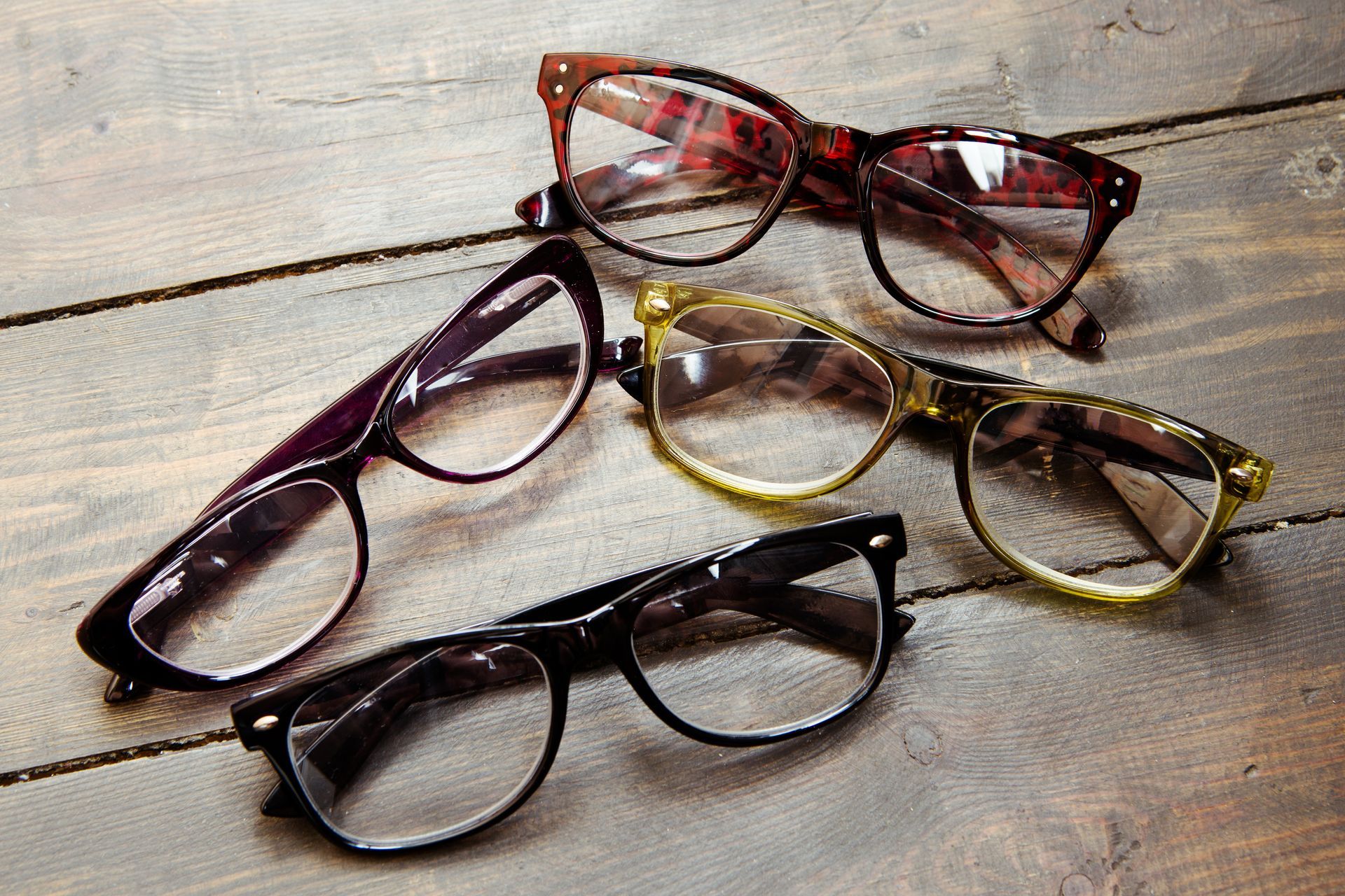 Three pairs of eyeglasses in brown, amber, and black on a rustic wooden surface Three pairs of eyeglasses in brown, amber, and black on a rustic wooden surface