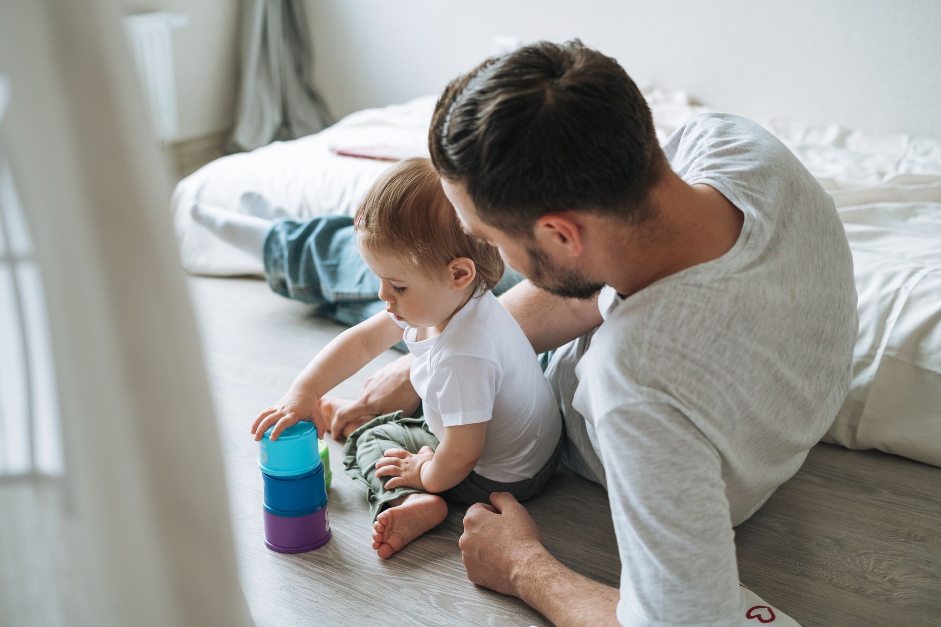 Father and toddler playing with stacking cups on the floor.