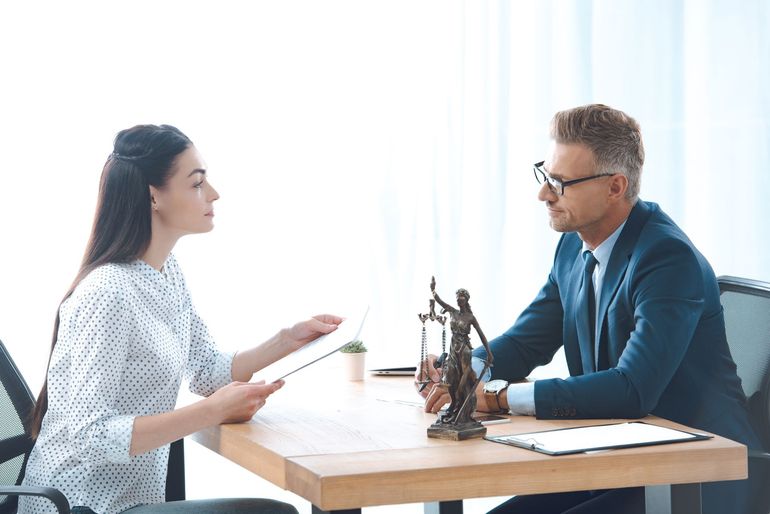 Woman and man in a meeting, reviewing documents at a table. Statute of Lady Justice present.