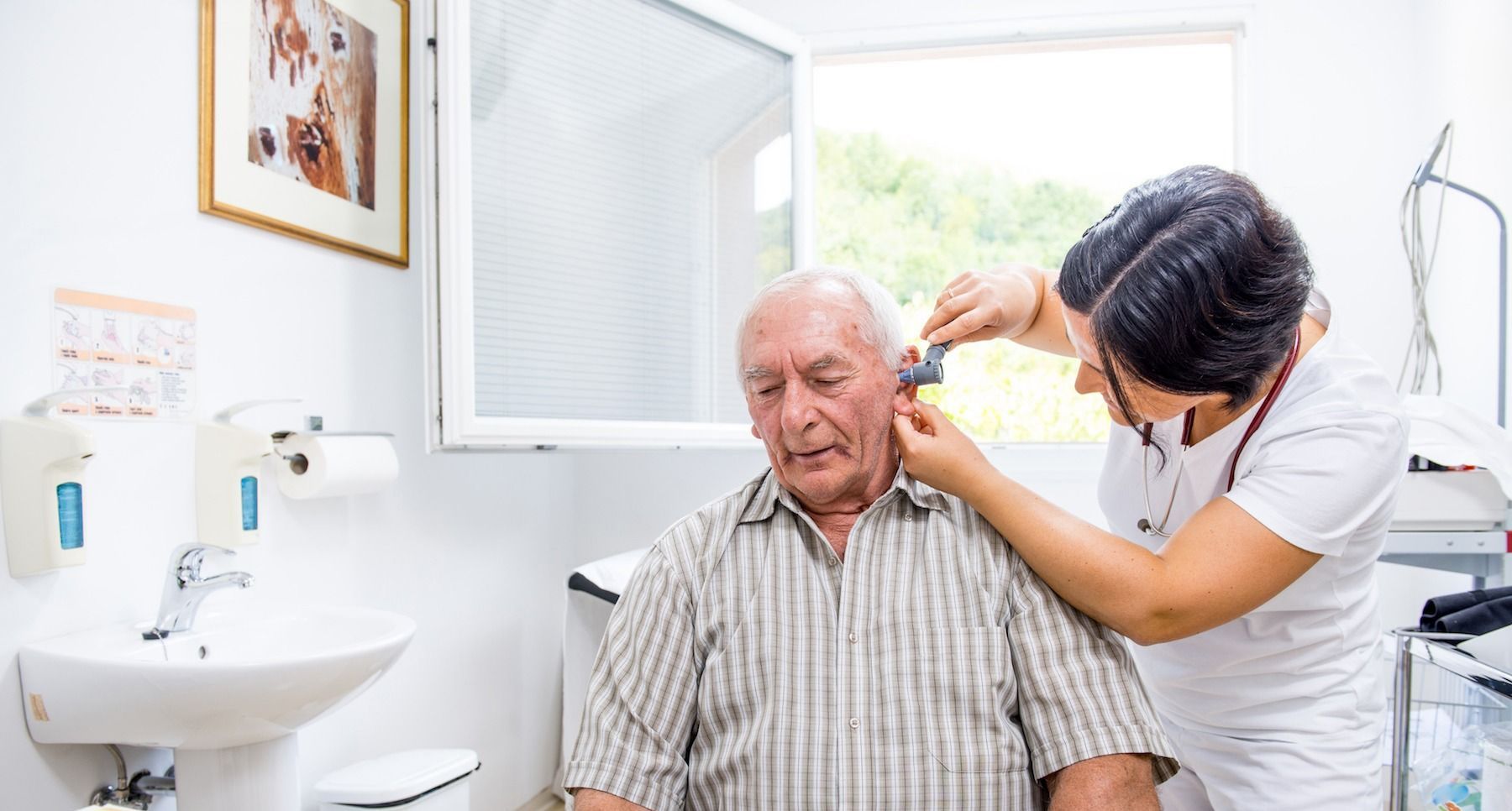 A nurse is examining an older man 's ear in a bathroom.