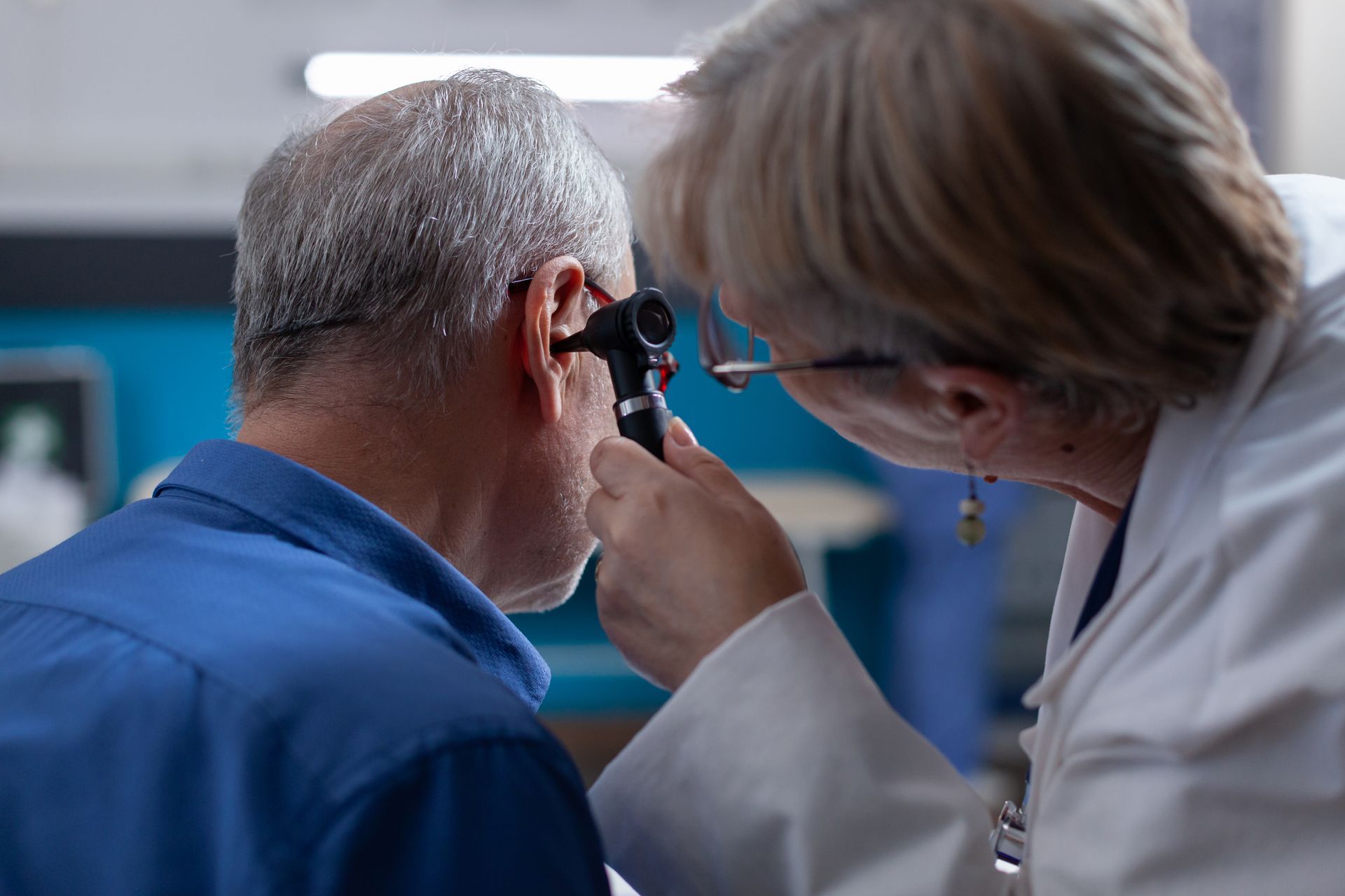 A doctor is examining an older man 's ear with an otoscope.