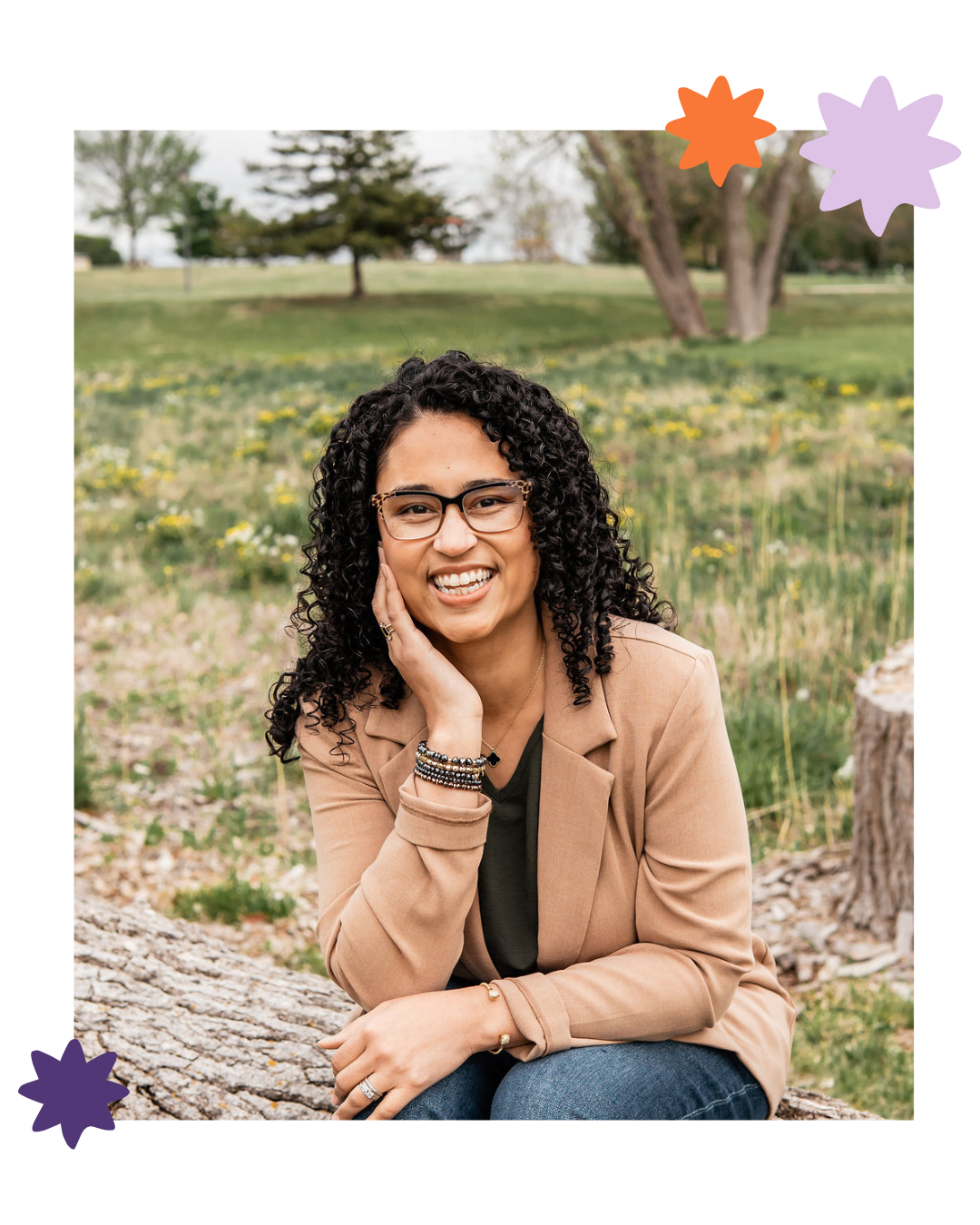 Smiling person sitting on a log in a grassy park, wearing a tan jacket and jeans, with decorative star stickers around the photo