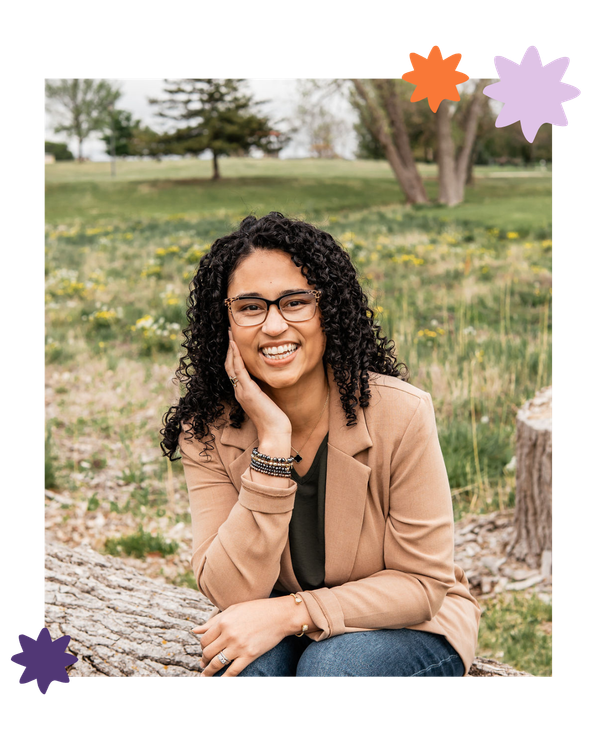 Smiling person sitting on a log in a grassy park, wearing a tan jacket and jeans, with decorative star stickers around the photo
