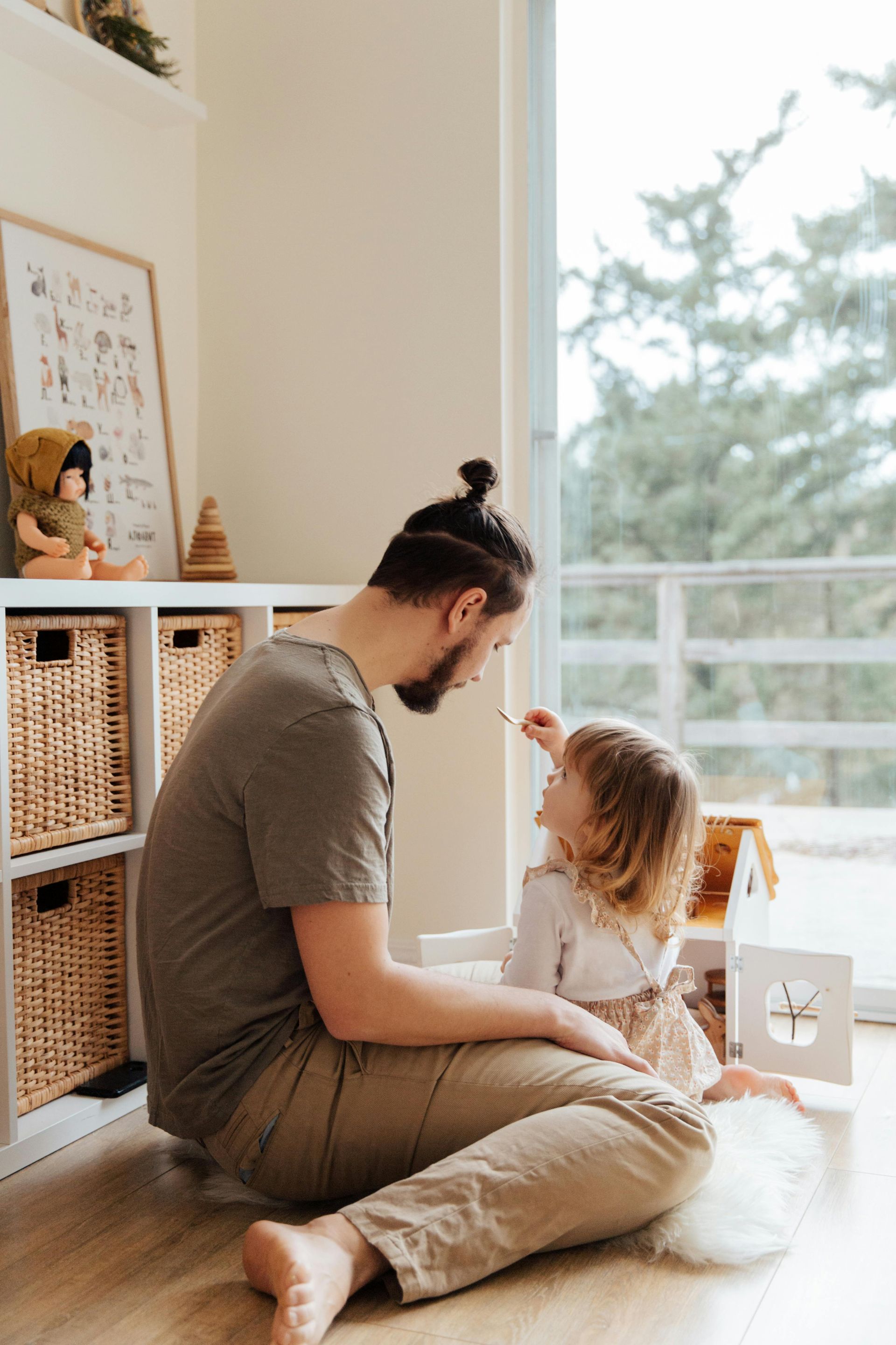 Parent and child sitting on the floor, facing each other in a bright playroom by a window
