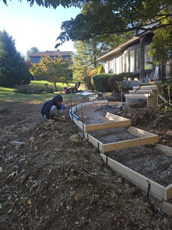 A person works on a curved wooden framework for new concrete steps in front of a house under construction.