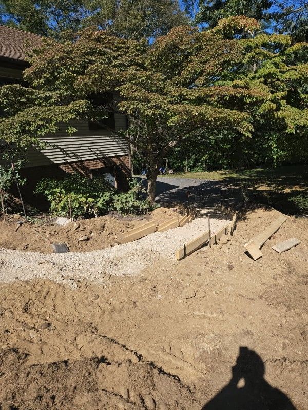 A yard under construction with a gravel walkway being framed by wooden boards leading toward a house.