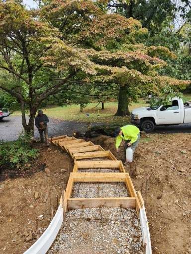 Two people working on a curved set of wooden staircase forms on a dirt hillside, with a white truck parked in the background.