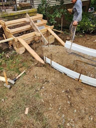 A worker prepares a form for concrete stairs and a walkway, using wooden stakes and boards in a dirt yard.