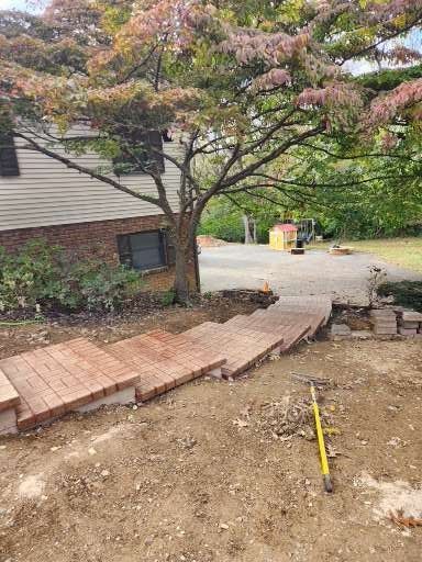A side view of newly installed wooden outdoor steps leading up a dirt slope toward a house with tan siding and a tree.
