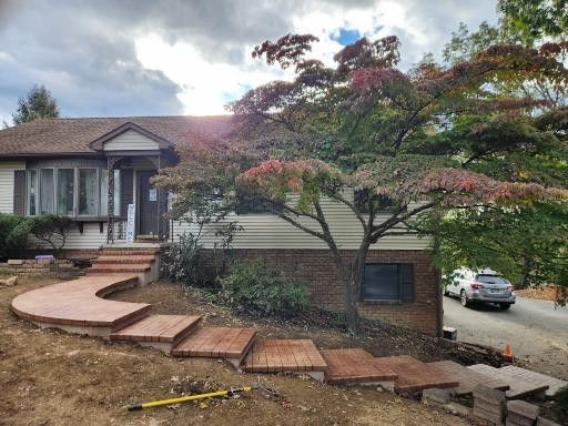 A house with new brick steps leading to the front porch, surrounded by bare dirt and a large Japanese maple tree.