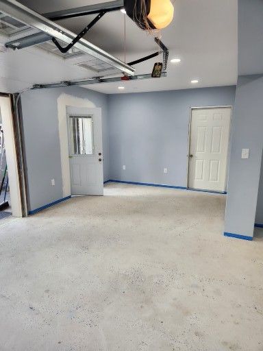 A clean, empty garage with light blue walls, a light-colored speckled floor, and two white doors.
