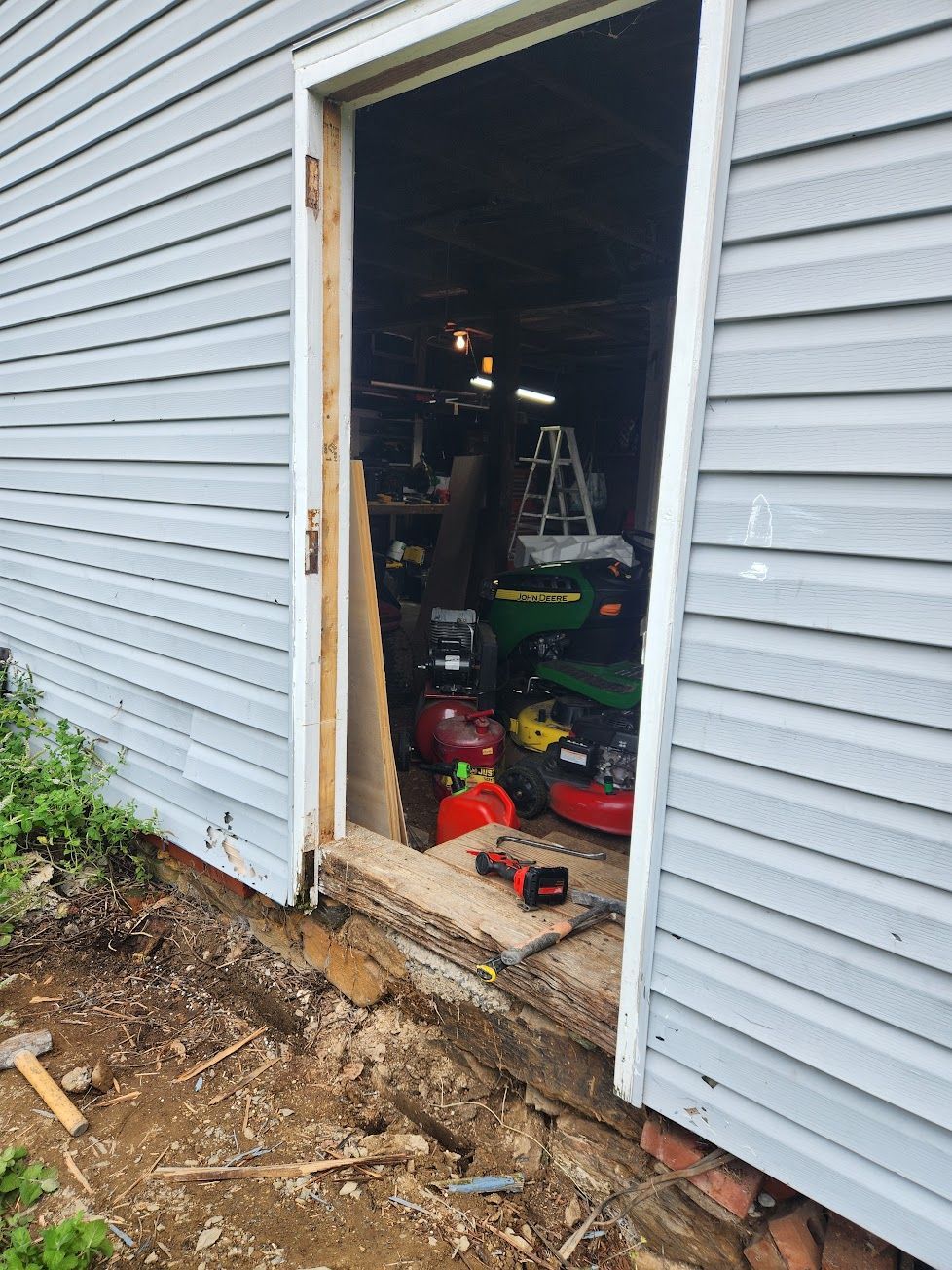 A light gray vinyl-sided building with an empty, unfinished doorway revealing a garage interior filled with tools.