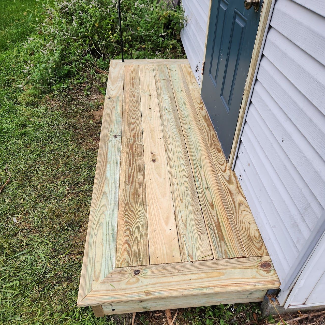 A wooden porch landing outside a building with light gray siding and a dark blue door.