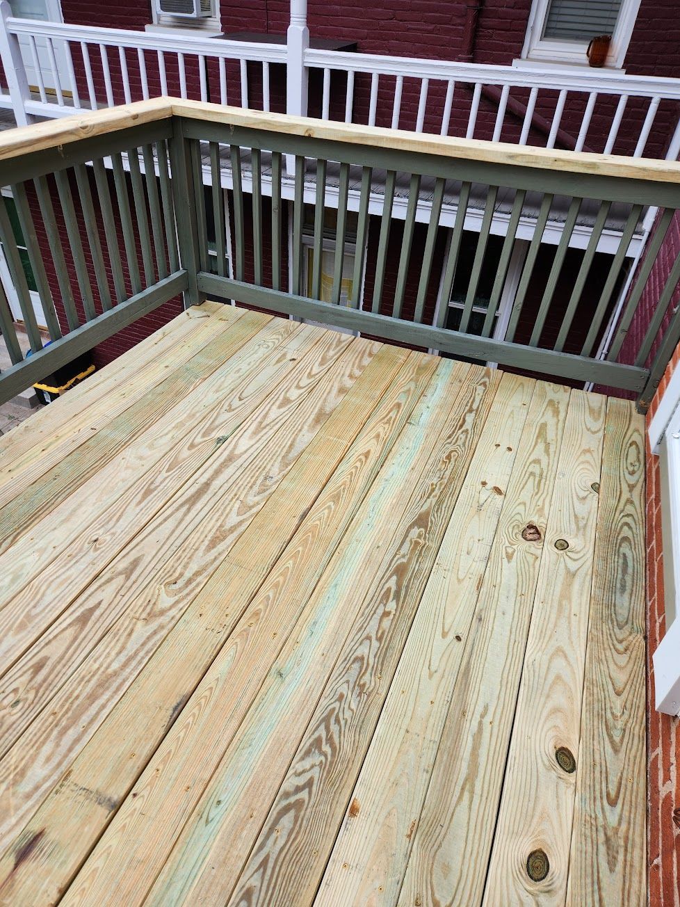 A newly built wooden deck with light-colored, pressure-treated planks and dark green railings against a brick house.