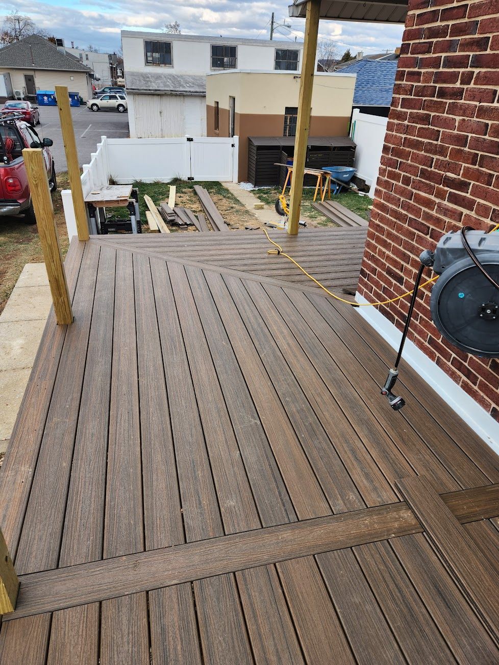 A newly built brown composite wood deck attached to a brick house, featuring wooden posts for railing.