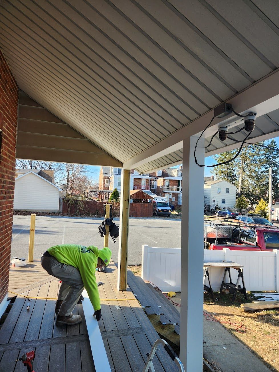 A construction worker in a lime-green shirt installs trim on the edge of a residential porch.