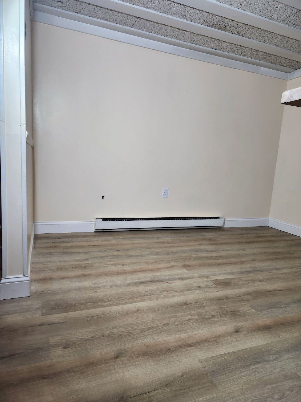 An empty room featuring light-colored walls, wood-look flooring, a baseboard heater, and a textured white ceiling.