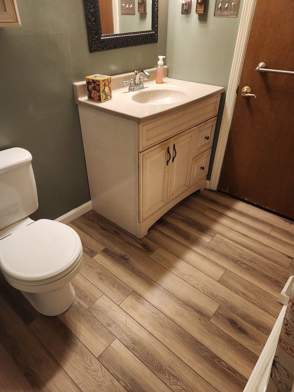 A small bathroom featuring a white vanity with a beige countertop, a toilet, and wood-look plank flooring.