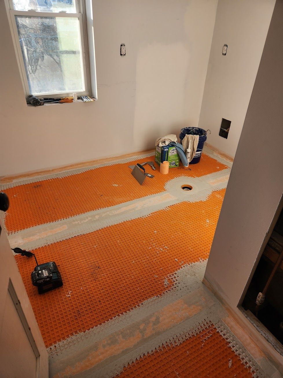A room under renovation with Schluter-DITRA orange uncoupling membrane installed on the floor around a central drain.