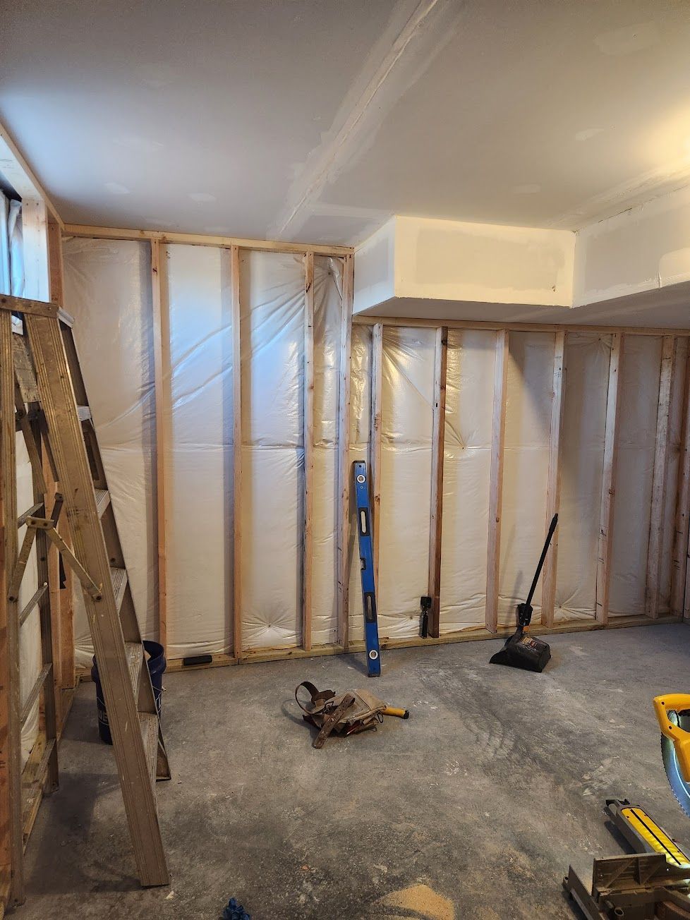 Interior view of a basement renovation with wood-framed walls, installed insulation, and construction tools on the floor.