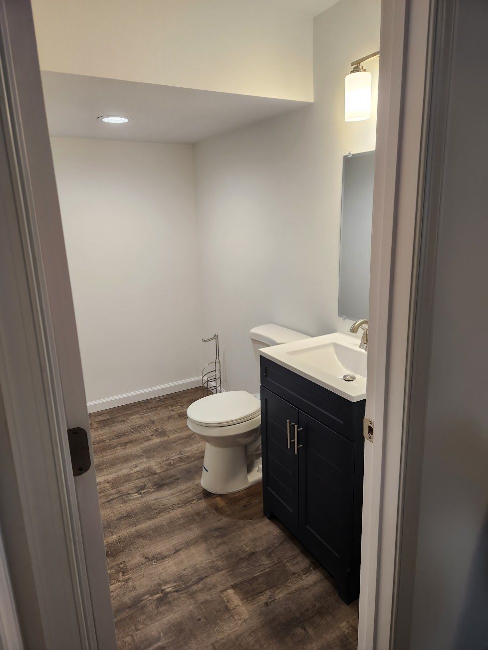 A bathroom featuring a navy vanity with a white sink, a toilet, and light-toned wood flooring.
