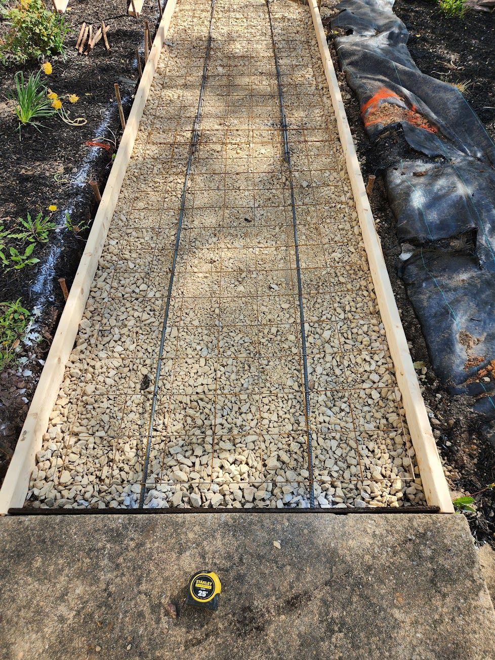 A narrow garden walkway under construction with wooden framing, a gravel base, and wire reinforcement mesh.