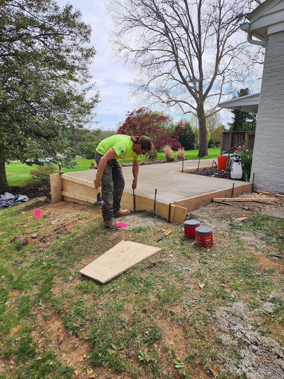 A worker in a neon yellow shirt installs wooden concrete forms for a patio project in a residential backyard.