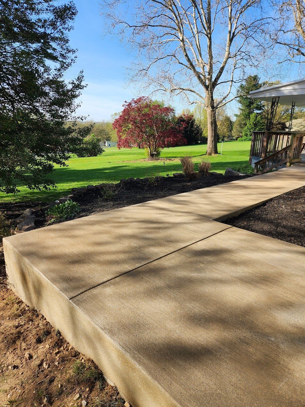 A concrete walkway leads through a grassy yard with trees under a clear blue sky.